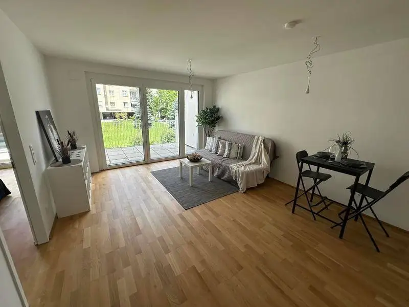 Lichtdurchfluteter Wohnbereich mit Holzboden und Blick ins Grüne durch große Fenster.