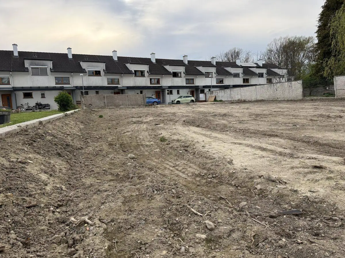 Weitläufiges Baugrundstück mit Blick auf eine Reihe von Reihenhäusern und viel Grün.