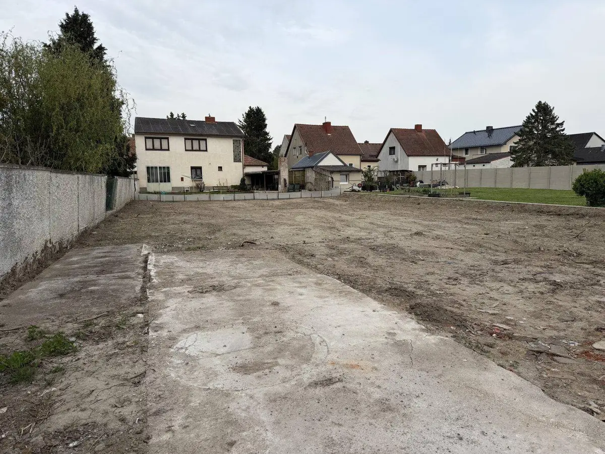 Baugrundstück mit Betonfundament und Blick auf die Nachbarschaft in grüner Umgebung.